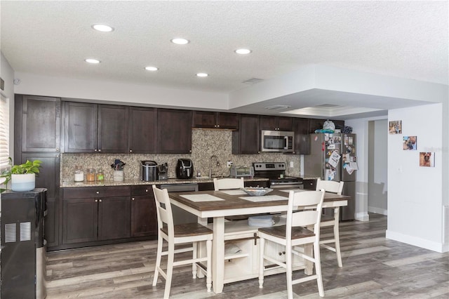 kitchen with backsplash, dark brown cabinets, a textured ceiling, stainless steel appliances, and wood-type flooring