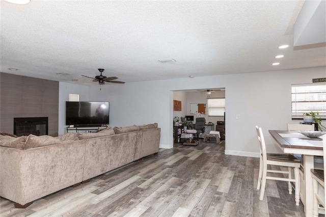 living room featuring a large fireplace, ceiling fan, hardwood / wood-style floors, and a textured ceiling