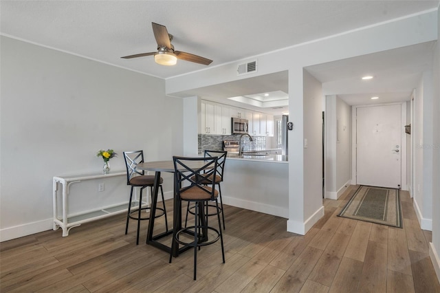 dining area featuring a raised ceiling, ceiling fan, sink, and hardwood / wood-style flooring