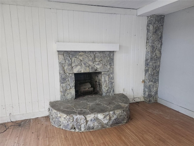 room details featuring beam ceiling, hardwood / wood-style flooring, a stone fireplace, and wooden walls