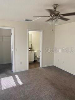 unfurnished bedroom featuring ensuite bathroom, ceiling fan, dark colored carpet, a spacious closet, and a closet