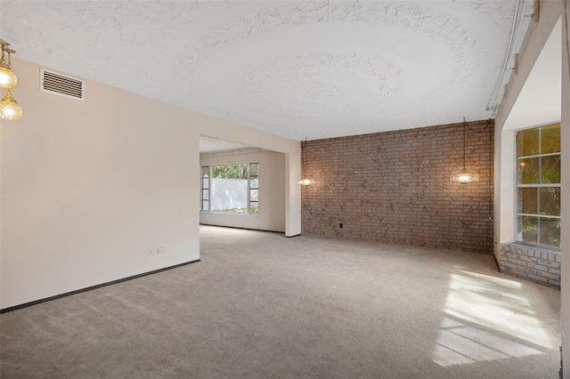 carpeted empty room featuring brick wall and a textured ceiling