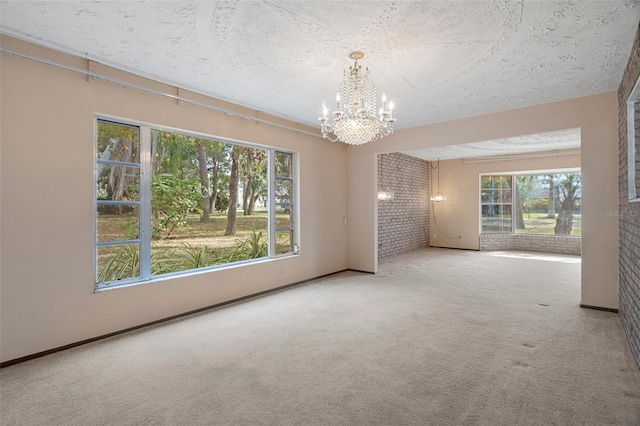 spare room with carpet flooring, a textured ceiling, brick wall, and a chandelier