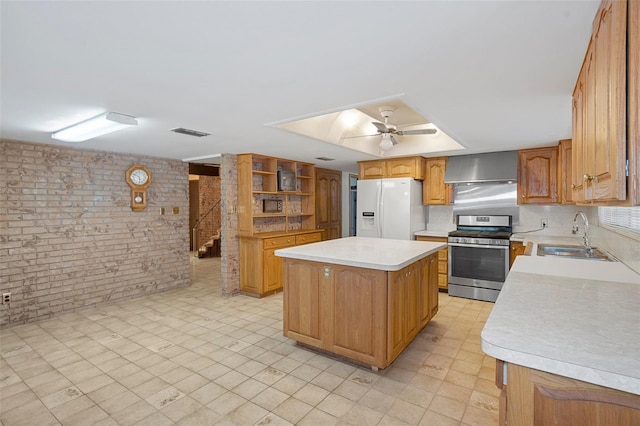 kitchen with gas range, wall chimney exhaust hood, brick wall, white refrigerator with ice dispenser, and a kitchen island