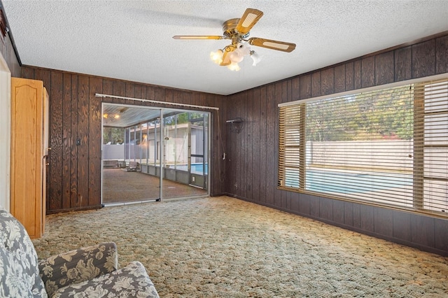 carpeted empty room with ceiling fan, wood walls, and a textured ceiling