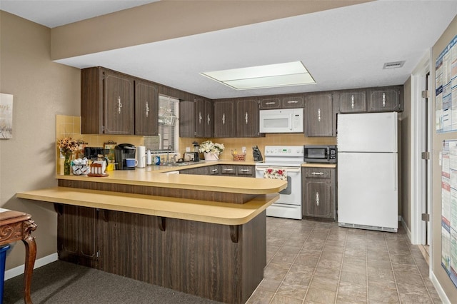 kitchen with kitchen peninsula, a kitchen breakfast bar, white appliances, dark brown cabinetry, and sink