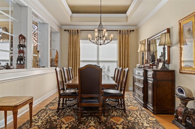 dining space with light wood-type flooring, crown molding, a tray ceiling, and a chandelier