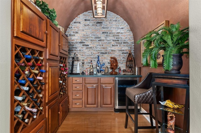 wine cellar with lofted ceiling, indoor bar, beverage cooler, and light hardwood / wood-style flooring