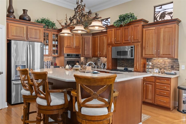 kitchen with stainless steel appliances, light hardwood / wood-style flooring, hanging light fixtures, and an island with sink