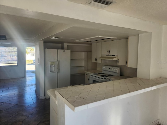 kitchen with tile countertops, white appliances, kitchen peninsula, a textured ceiling, and white cabinetry