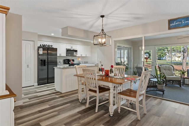 dining area with ceiling fan with notable chandelier, wood-type flooring, and a textured ceiling