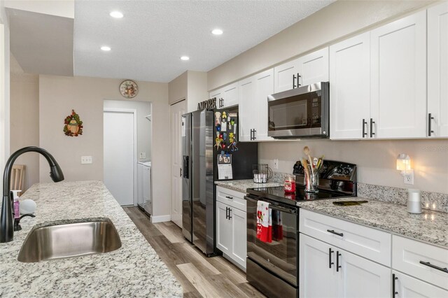 kitchen featuring white cabinets, sink, light hardwood / wood-style floors, light stone counters, and stainless steel appliances