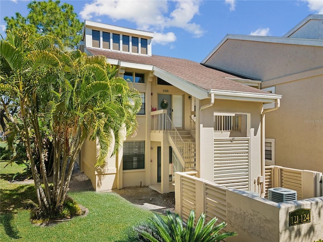 exterior space featuring a shingled roof, stairway, fence, cooling unit, and stucco siding