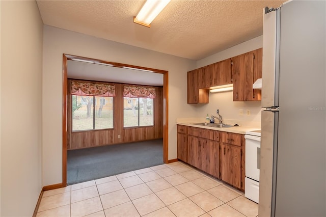 kitchen featuring a textured ceiling, white appliances, sink, light tile patterned floors, and range hood