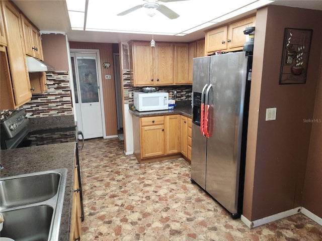 kitchen with under cabinet range hood, a sink, appliances with stainless steel finishes, backsplash, and dark countertops