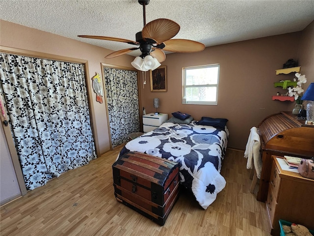 bedroom featuring multiple closets, light wood-style floors, ceiling fan, and a textured ceiling