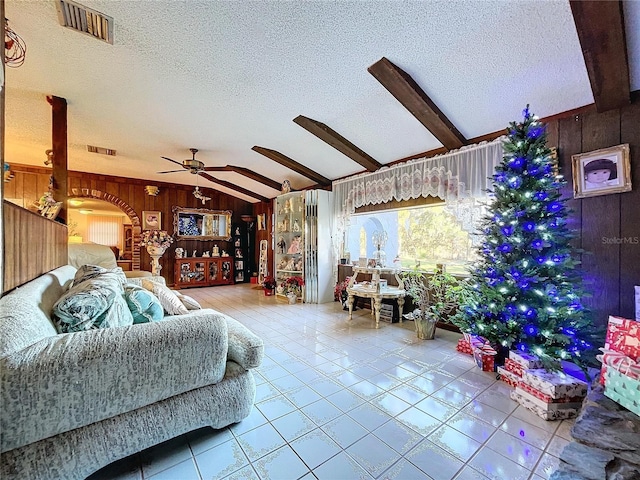 tiled living room featuring wooden walls, ceiling fan, lofted ceiling with beams, and a textured ceiling