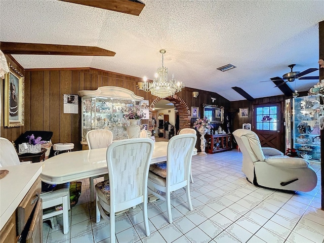 dining area with ceiling fan with notable chandelier, a textured ceiling, vaulted ceiling with beams, and wooden walls