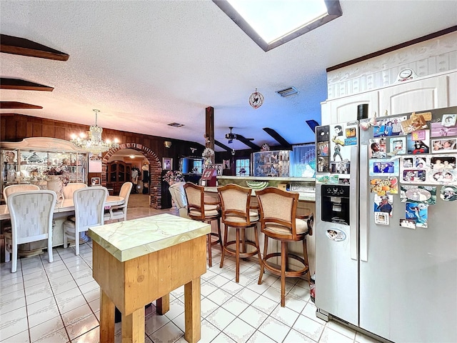 kitchen with ceiling fan with notable chandelier, stainless steel refrigerator with ice dispenser, wooden walls, light tile patterned floors, and a textured ceiling