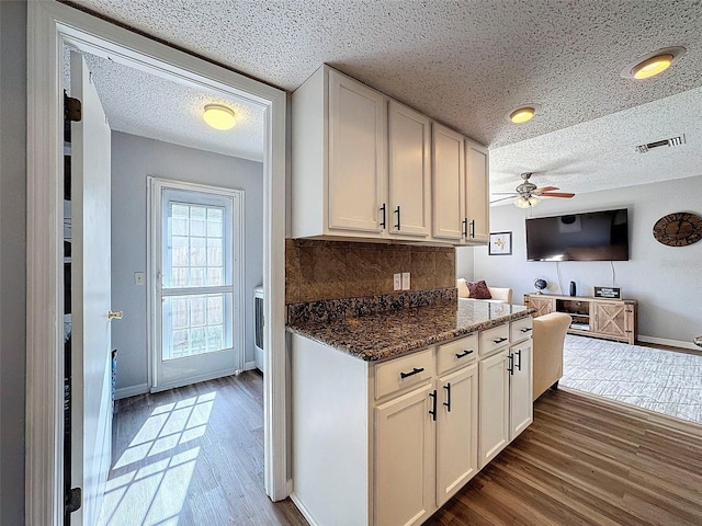 kitchen featuring dark stone counters, dark wood-type flooring, ceiling fan, white cabinets, and tasteful backsplash