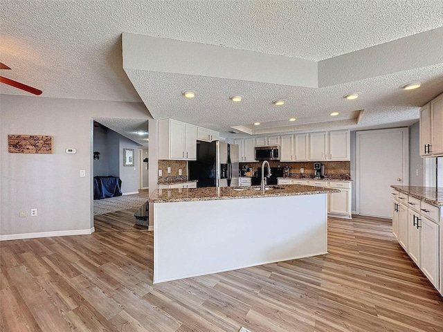 kitchen featuring a kitchen island with sink, stainless steel appliances, dark stone counters, sink, and white cabinetry