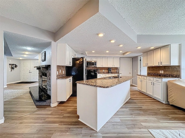 kitchen featuring sink, white cabinets, dark stone countertops, black appliances, and a kitchen island with sink