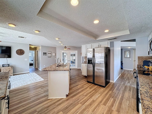 kitchen with a center island with sink, light stone counters, stainless steel refrigerator with ice dispenser, white cabinets, and sink