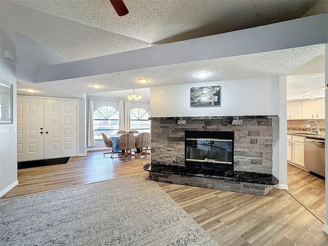 living room featuring sink, a fireplace, vaulted ceiling, light hardwood / wood-style flooring, and ceiling fan with notable chandelier