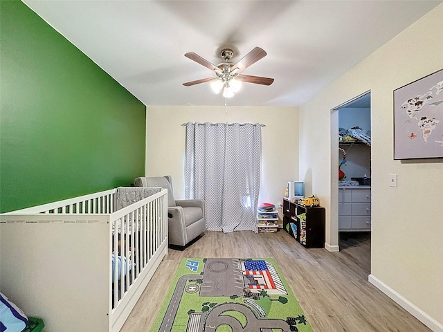 unfurnished bedroom with a nursery area, a walk in closet, ceiling fan, and light hardwood / wood-style flooring