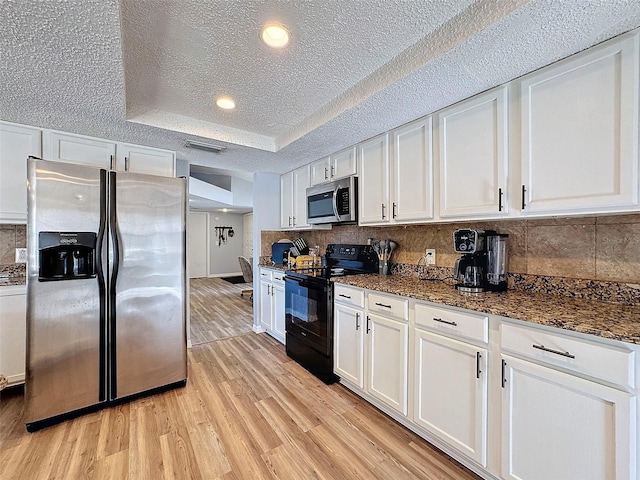 kitchen featuring stainless steel appliances, white cabinetry, tasteful backsplash, light hardwood / wood-style flooring, and a tray ceiling