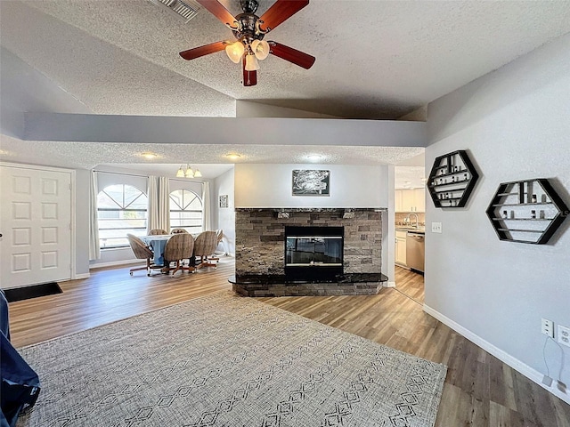 living room with sink, a textured ceiling, vaulted ceiling, hardwood / wood-style floors, and a stone fireplace