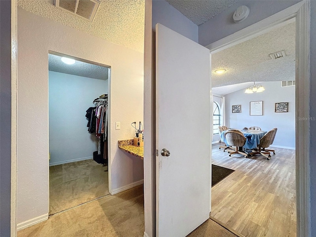 hallway featuring a textured ceiling, hardwood / wood-style floors, lofted ceiling, and a chandelier