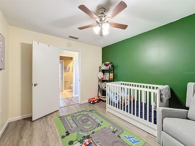 bedroom featuring ceiling fan, light hardwood / wood-style flooring, and a nursery area