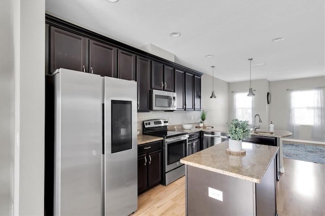 kitchen with tasteful backsplash, stainless steel appliances, decorative light fixtures, light hardwood / wood-style flooring, and a center island