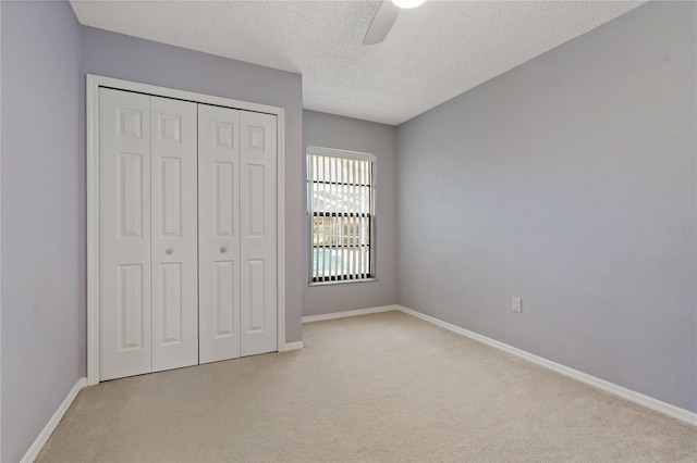 unfurnished bedroom featuring light carpet, a textured ceiling, a closet, and ceiling fan