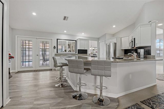 kitchen featuring a breakfast bar area, stainless steel appliances, white cabinets, french doors, and kitchen peninsula