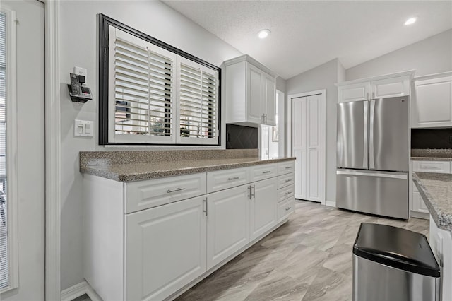 kitchen with white cabinetry, lofted ceiling, stainless steel fridge, and light stone counters