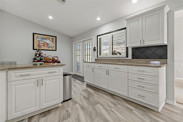 kitchen with white cabinetry, light stone counters, tasteful backsplash, and lofted ceiling