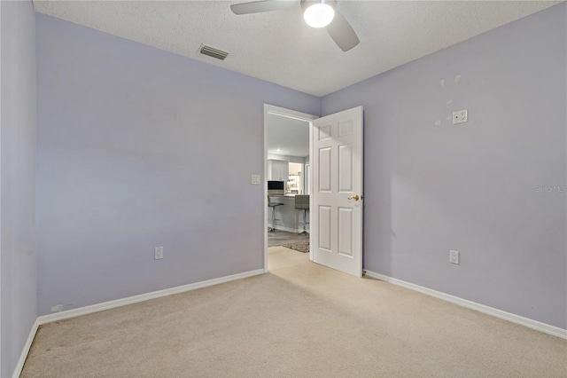 empty room with light colored carpet, a textured ceiling, and ceiling fan