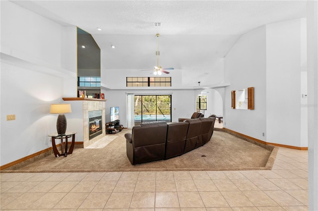 living room with high vaulted ceiling, ceiling fan, light tile patterned floors, a textured ceiling, and a tiled fireplace