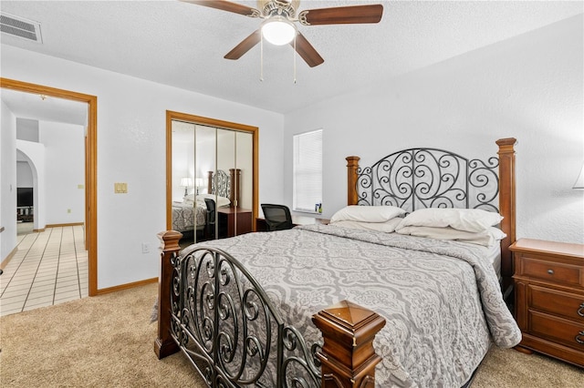 bedroom featuring a textured ceiling, a closet, light colored carpet, and ceiling fan