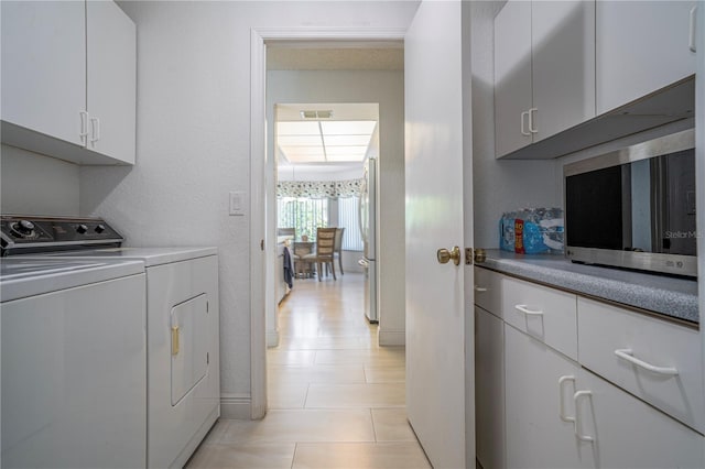 clothes washing area with cabinets, independent washer and dryer, and light tile patterned floors