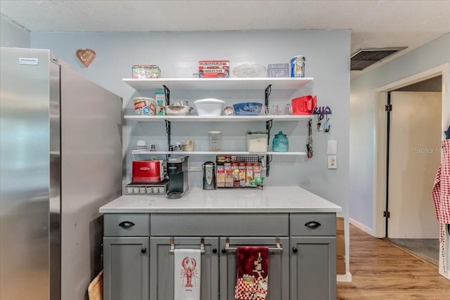 bar with light stone countertops, gray cabinetry, stainless steel refrigerator, and light hardwood / wood-style floors