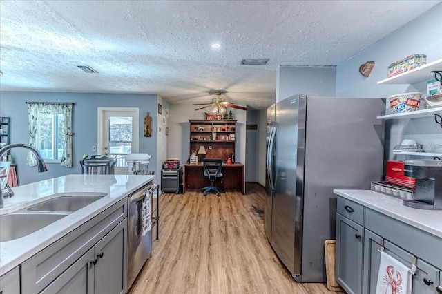 kitchen with a textured ceiling, appliances with stainless steel finishes, light hardwood / wood-style floors, sink, and gray cabinetry