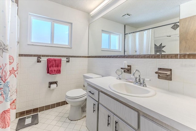 bathroom with a textured ceiling, tile patterned flooring, vanity, tile walls, and toilet