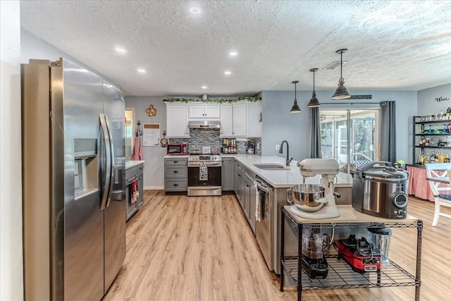 kitchen with kitchen peninsula, appliances with stainless steel finishes, hanging light fixtures, white cabinets, and sink