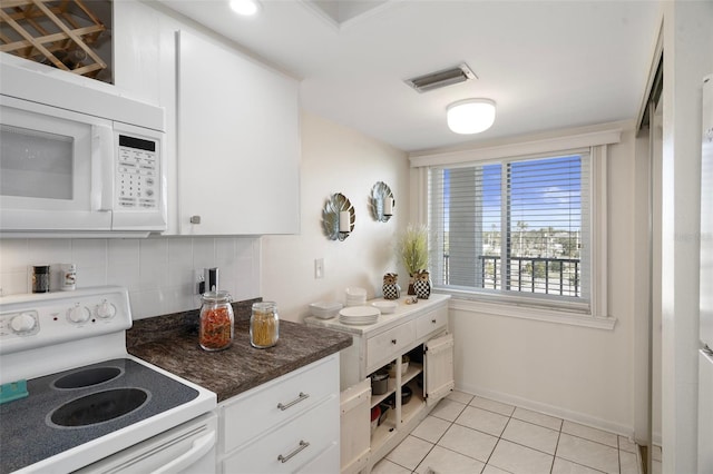 kitchen with white appliances, backsplash, dark stone counters, light tile patterned floors, and white cabinetry