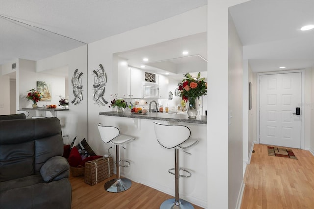 bar with tasteful backsplash, white cabinetry, light hardwood / wood-style flooring, and sink