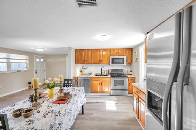 kitchen with appliances with stainless steel finishes, a textured ceiling, light hardwood / wood-style flooring, and sink