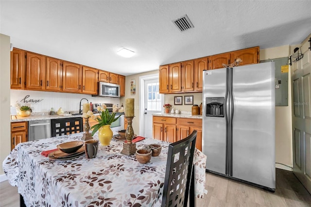 kitchen with appliances with stainless steel finishes, a textured ceiling, and light hardwood / wood-style floors